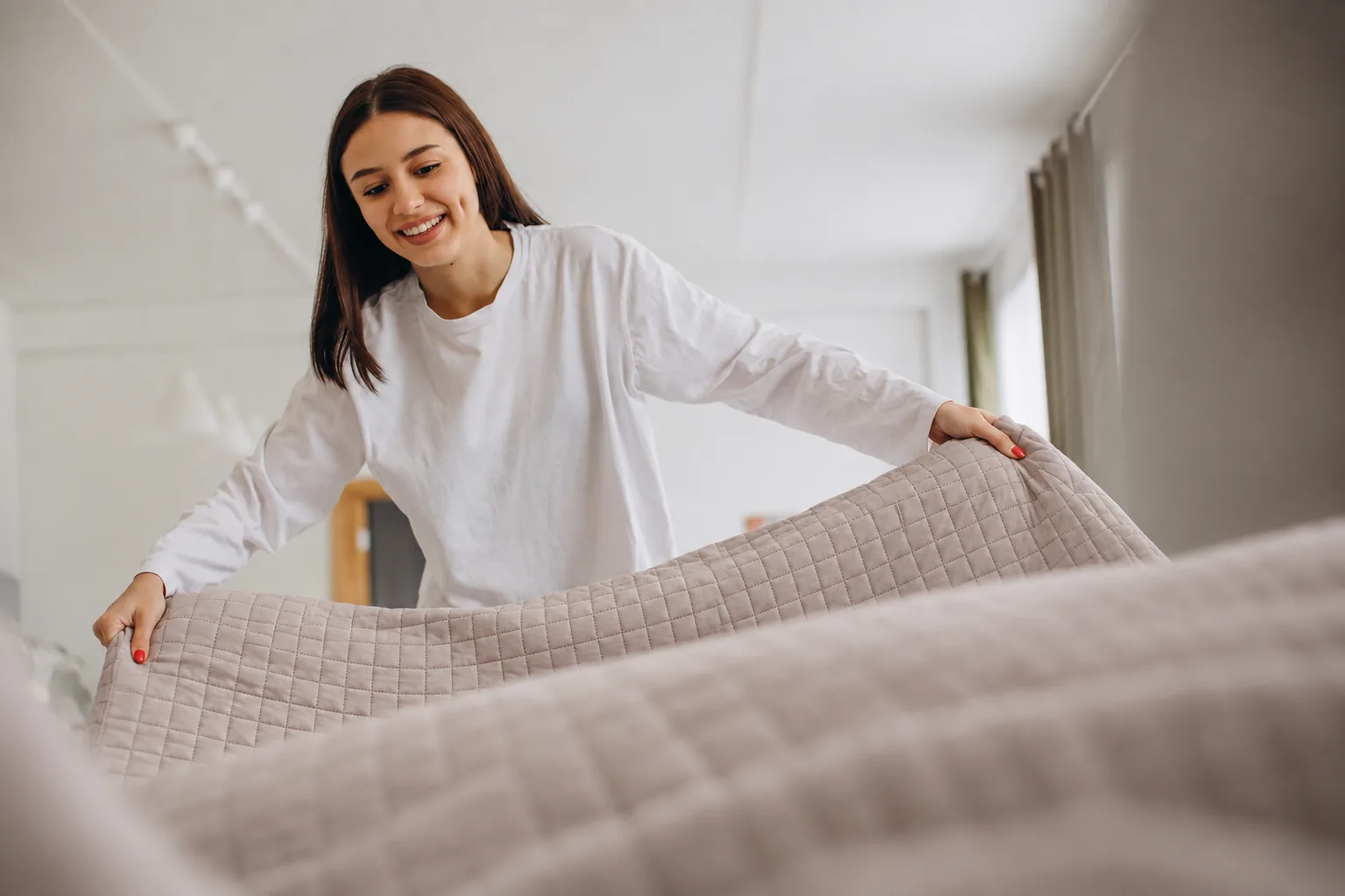 Mulher arrumando a cama durante uma etapa da organização do quarto.